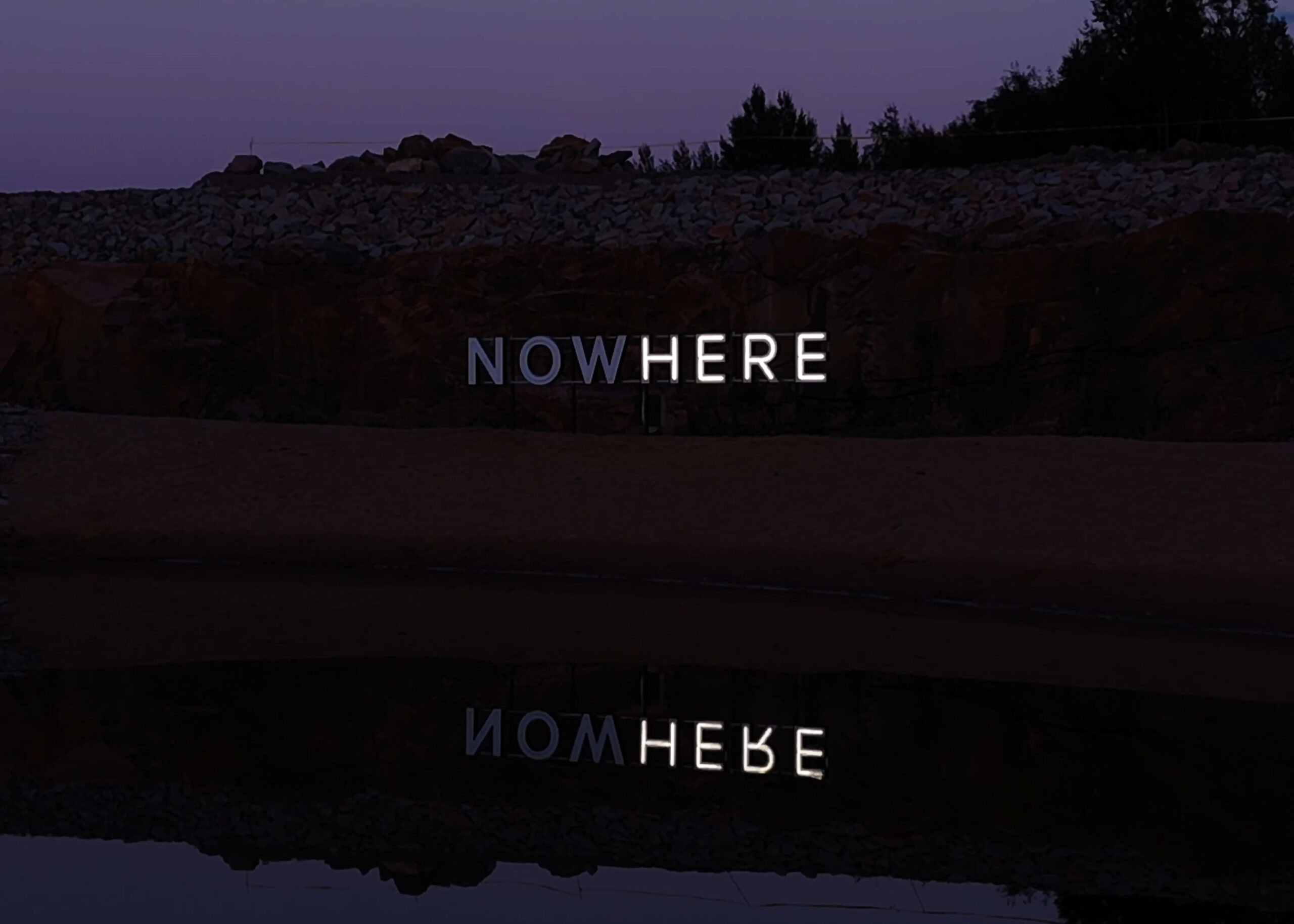 NOW/HERE, kinetic neon work by Timo Aho: neon letters glow white with only [some letters / the word "HERE"] lit at this moment.